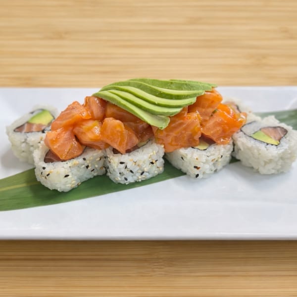 Sushi rolls topped with diced salmon and sliced avocado, served on a white plate with a green leaf.