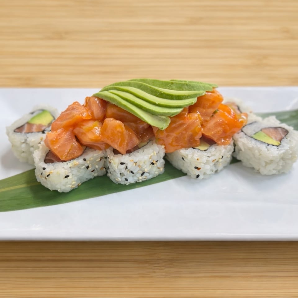 Sushi rolls topped with diced salmon and sliced avocado, served on a white plate with a green leaf.
