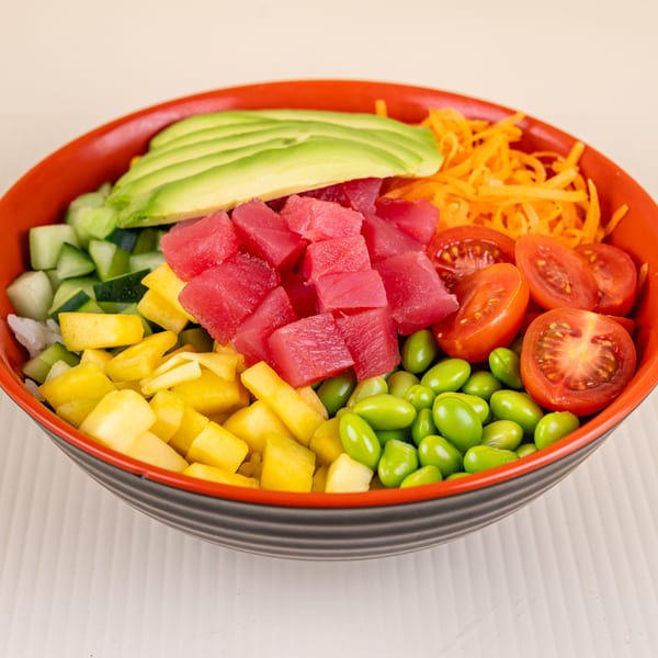 Colorful poke bowl with tuna, avocado, mango, edamame, tomatoes, cucumber, and carrots.