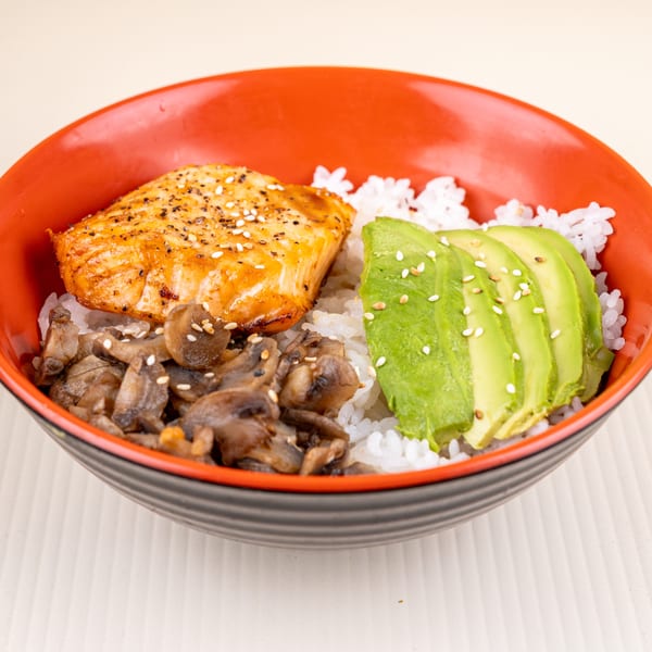 Salmon, mushrooms, and avocado slices over white rice in a red and black bowl.
