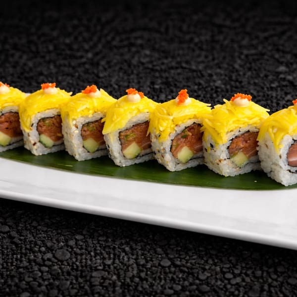 Sushi rolls with yellow mango topping, orange roe, and white sauce on a banana leaf.