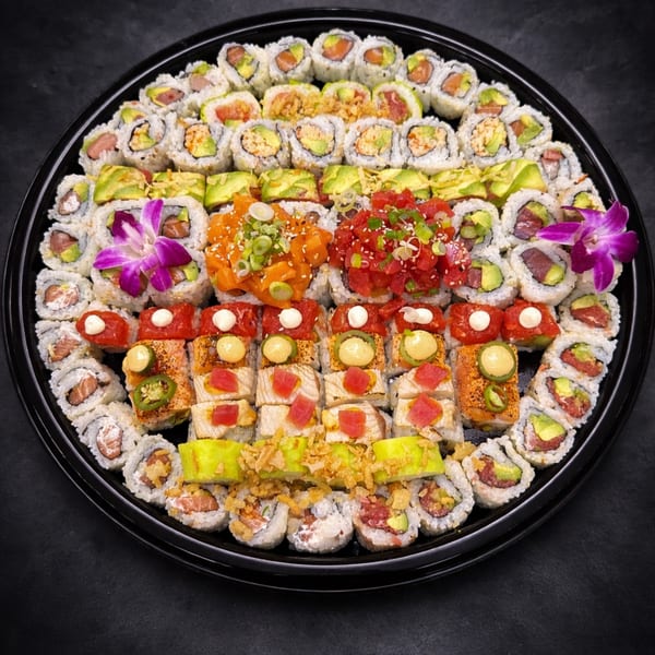 Large black platter filled with various sushi rolls, sashimi, and two purple orchid garnishes.