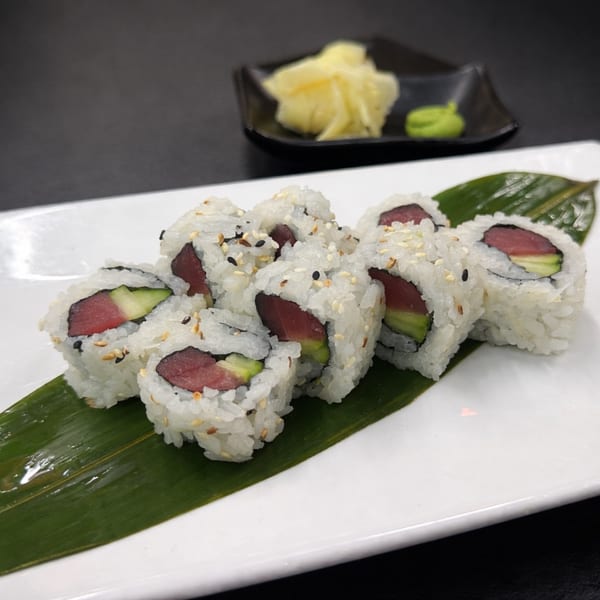 Tuna and avocado sushi rolls on a white plate with a green leaf, ginger, and wasabi.