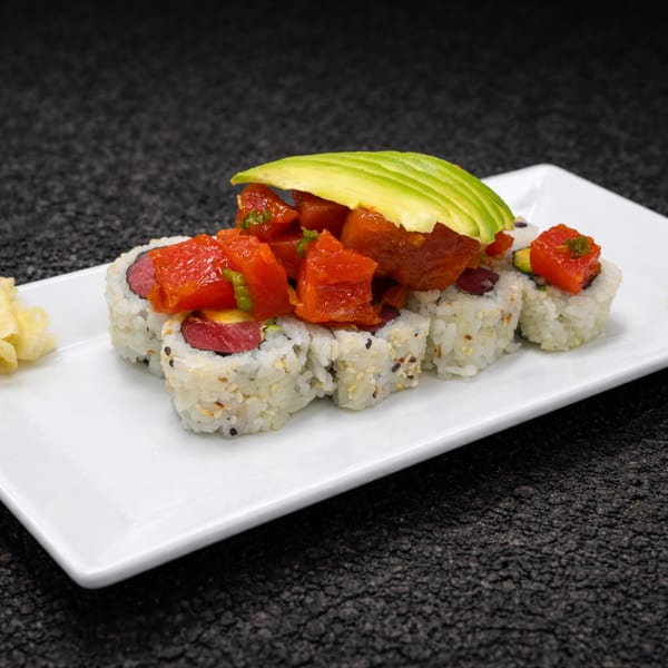 Sushi rolls topped with diced tuna and sliced avocado, served on a white rectangular plate.