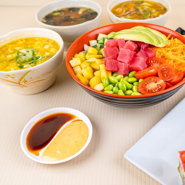 A colorful poke bowl with tuna, avocado, and edamame, alongside three bowls of soup and dipping sauces.